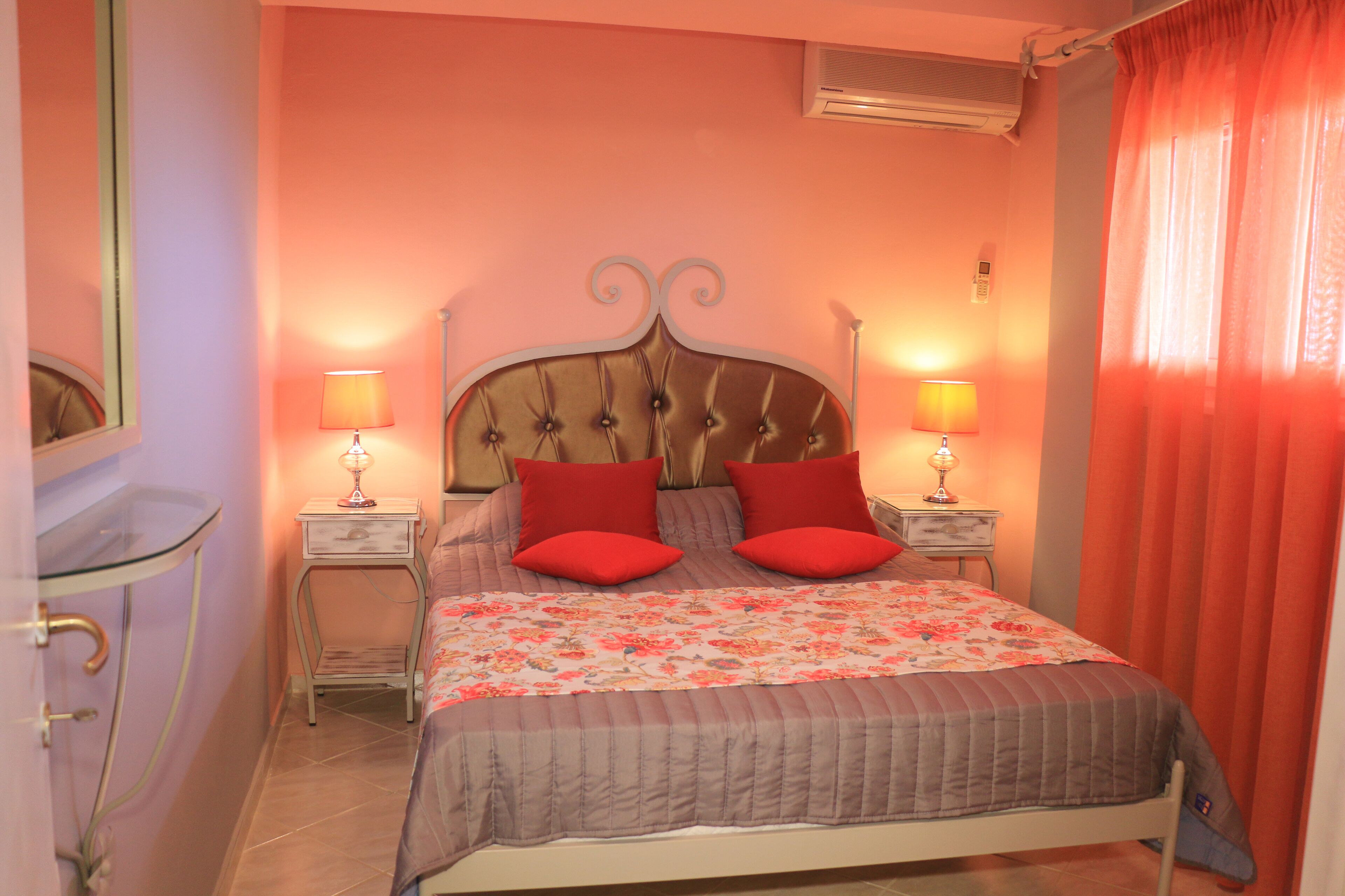 Un dormitorio con una cama, dos mesitas de noche, un espejo y una ventana con cortinas.