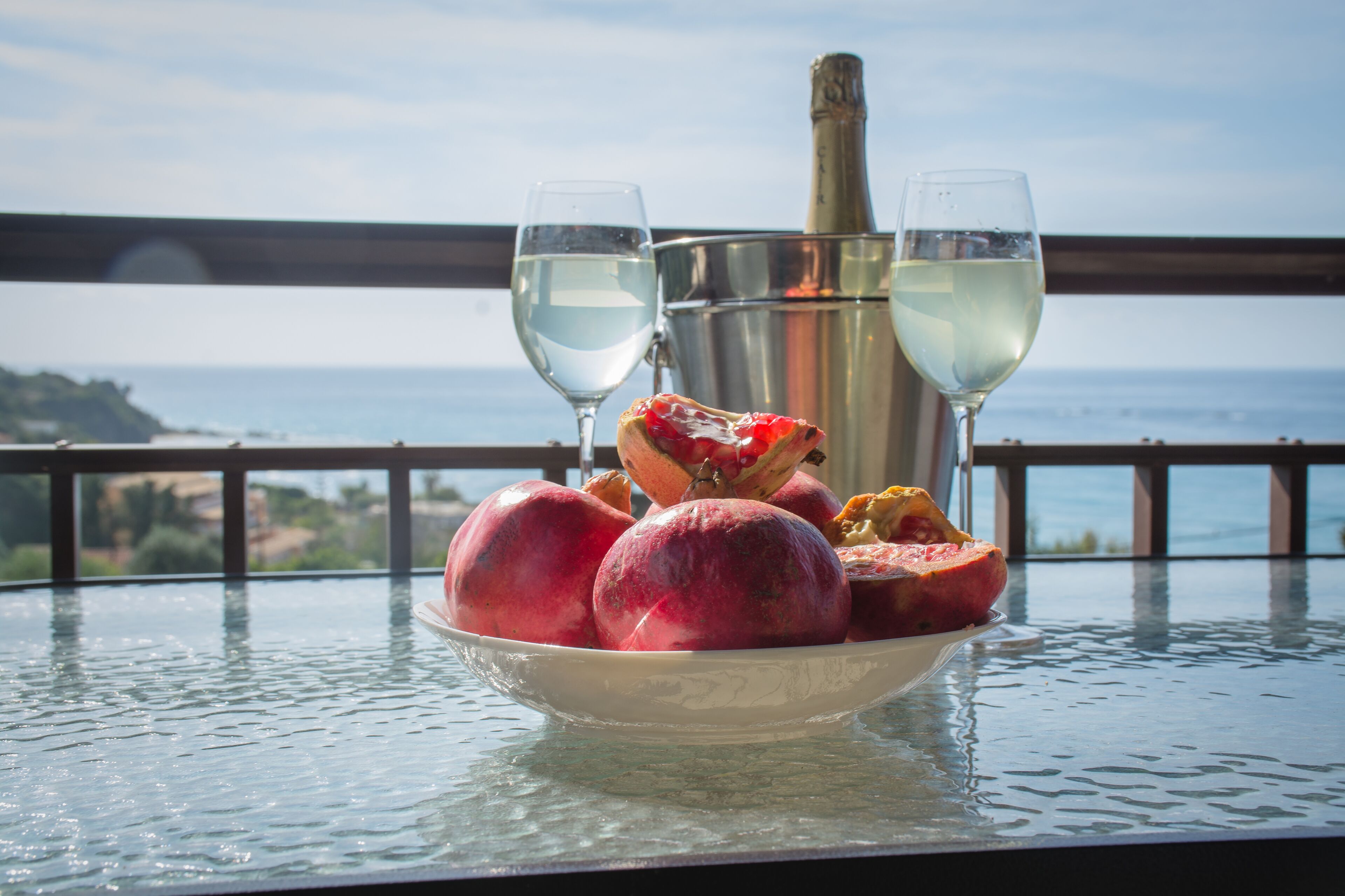 A table with a bowl of fruit, two glasses of white wine, and a champagne bottle.