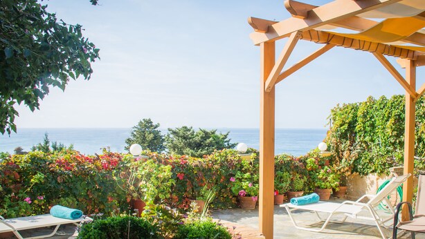 A covered outdoor seating area with a view of the sea, surrounded by potted plants and flowers. - Villa Aris - Holiday & relaxation (Corfu - Kerkyra)