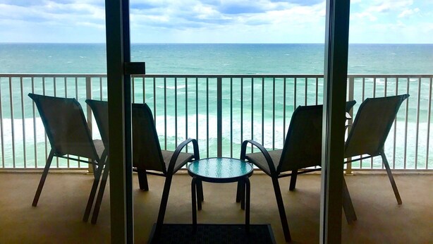 En balkon med to stole og et lille bord, med udsigt over havet.