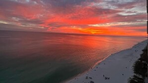 En strand med solnedgang, rolig sø og klar himmel.