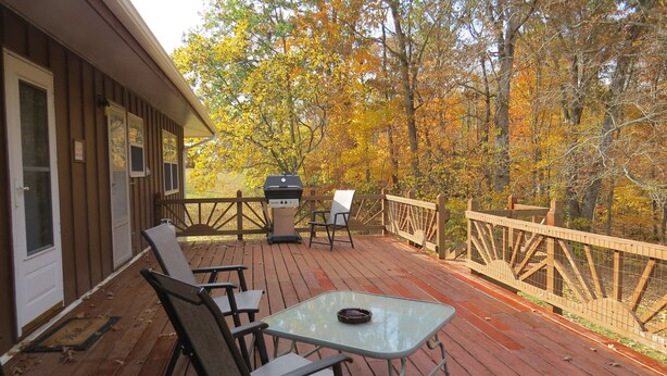 A wooden deck with outdoor seating, a grill, and a view of autumn trees.