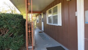 A covered porch with a metal railing, a door, and a window with shutters.