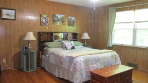 A bedroom with wooden paneling, a bed with floral bedding, two bedside lamps, a wooden chest of drawers, and a ceiling fan.