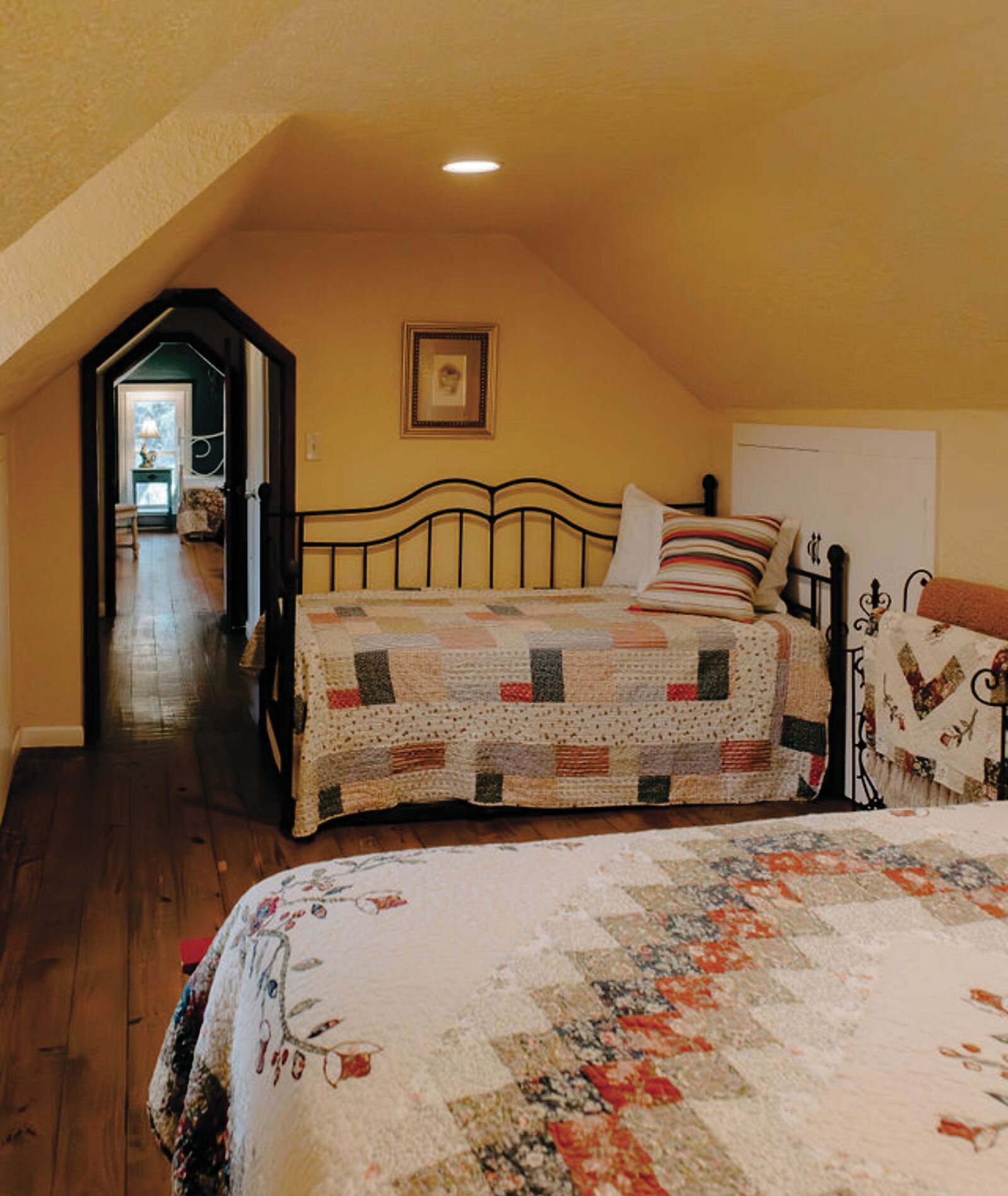 Un dormitorio con dos camas, suelo de madera, un cuadro en la pared y un pasillo que conduce a otra habitación.