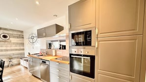 A modern kitchen with stainless steel appliances, a wooden countertop, and a compass wall decoration. - The wind rose 8 people (Grandcamp-Maisy)