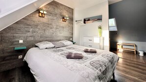 A modern bedroom with a sloped ceiling, a bed with a clock-themed duvet, a nightstand, a dresser, and a TV on the wall. - The wind rose 8 people (Grandcamp-Maisy)