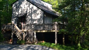A rustic cabin with a wooden deck and a staircase leading to a porch.