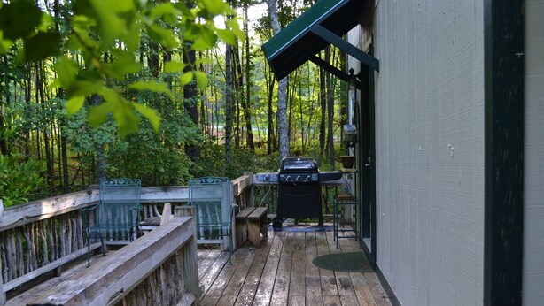 A wooden deck with a barbecue grill, a metal chair, and a wooden bench.