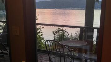 A dining area with a table and chairs, a candle on the table, and a view of a lake with mountains in the background.