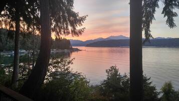 A lake with a dock and a sailboat, surrounded by trees and mountains in the background.