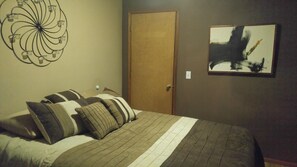 Une chambre à coucher avec un lit, des oreillers, une horloge murale, une porte et un tableau.