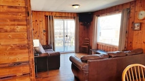 A cozy cabin-style room with a wooden interior, a sofa, a table, and a chair. - 2 Bedroom Cottage 100 yards to water. Dock & Ramp. (Lakeside Marblehead)