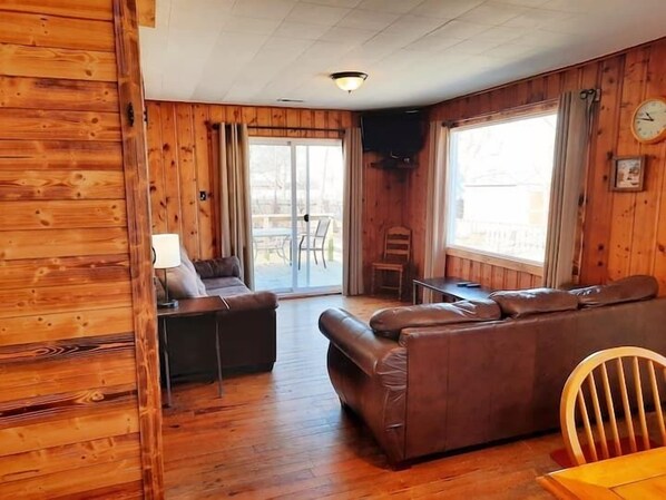 A cozy cabin-style room with a wooden interior, a sofa, a table, and a chair.