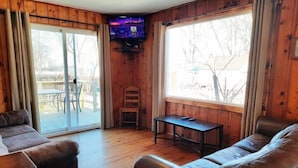 A room with a wooden interior, a sliding glass door leading outside, a television mounted on the wall, and two leather sofas. - 2 Bedroom Cottage 100 yards to water. Dock & Ramp. (Lakeside Marblehead)