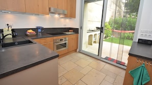 Een moderne keuken met houten kastjes, een ingebouwde oven en een grote schuifdeur die uitkomt op een terras.