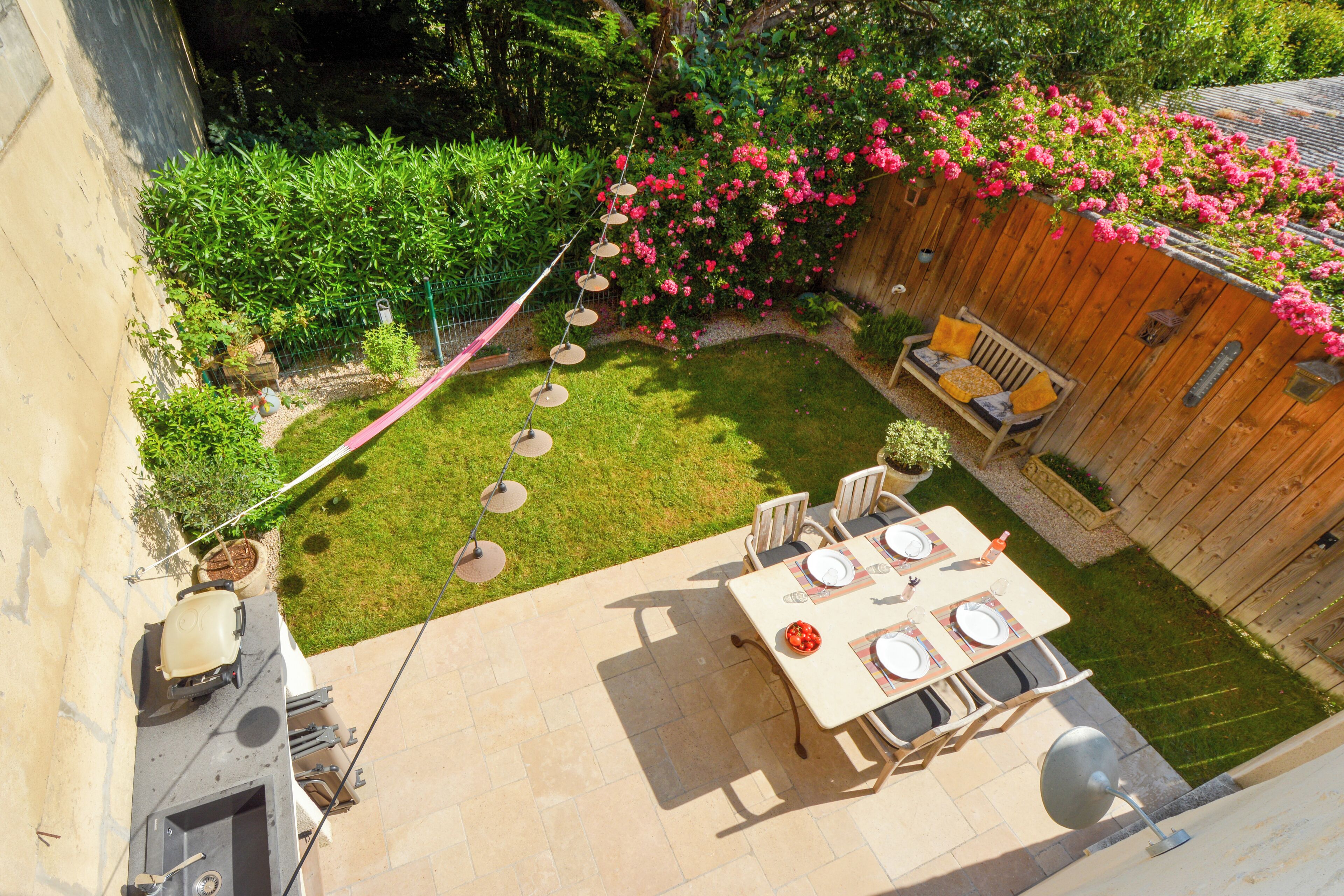 A patio with a table set for dining, surrounded by a wooden fence and lush greenery.