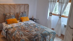 Een slaapkamer met een bed, twee nachtkastjes, een wandlamp en een raam met gordijnen.