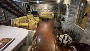 A cozy living room with a stone wall, a yellow sofa set, a dining table, and a staircase leading to an upper level.