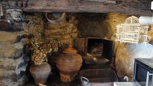 A rustic kitchen with a stone wall, a large clay pot, a metal pot, and a hanging birdcage.