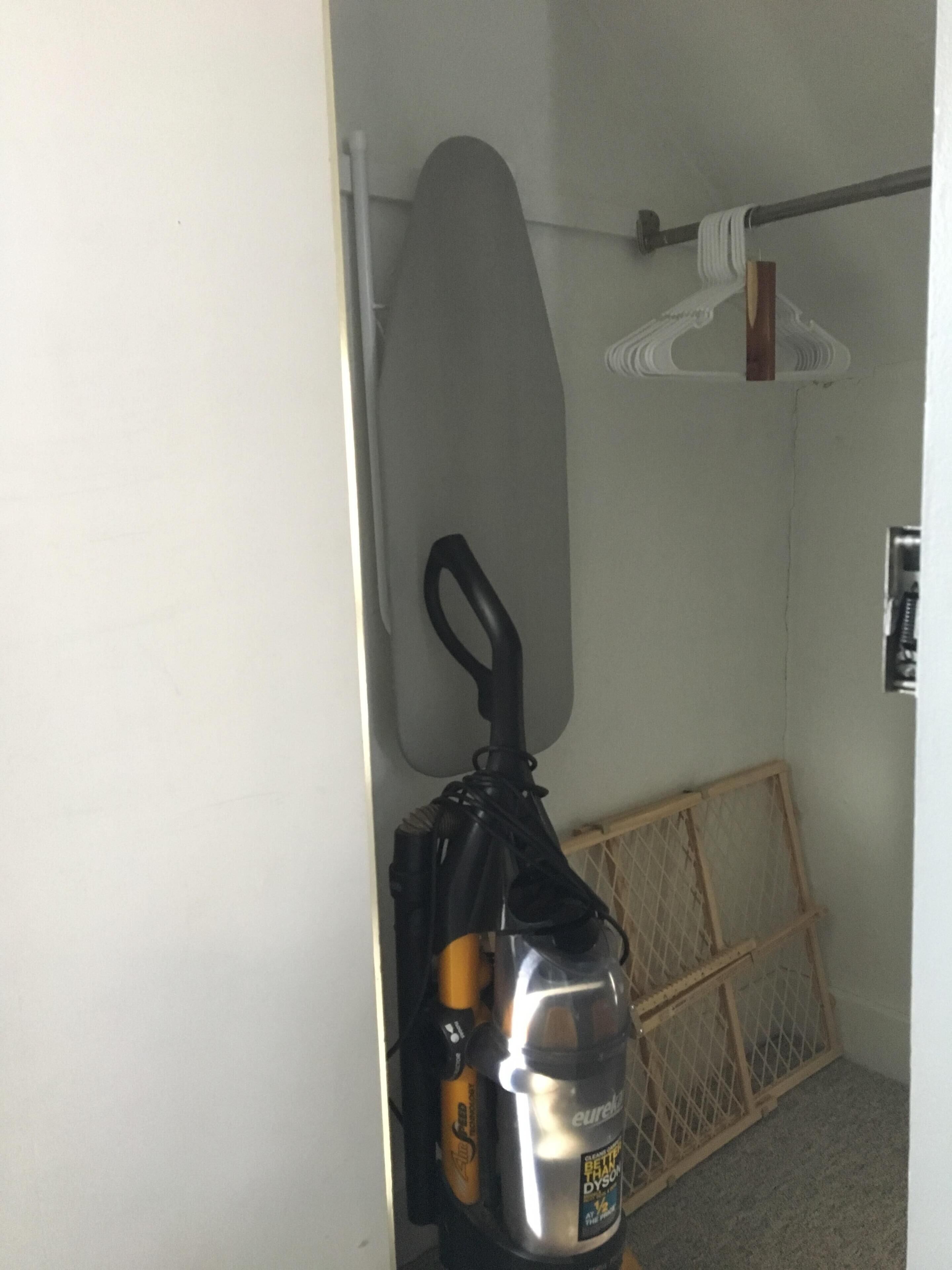 Een kamer met een surfboard tegen de muur, een stofzuiger en een houten kist.