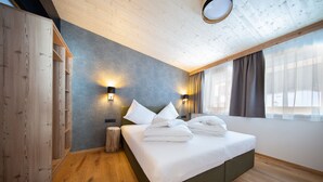 Une chambre d’hôtel moderne avec un plancher en bois, un grand lit avec du linge de lit blanc, deux lampes fixées au mur et une grande fenêtre avec des rideaux.