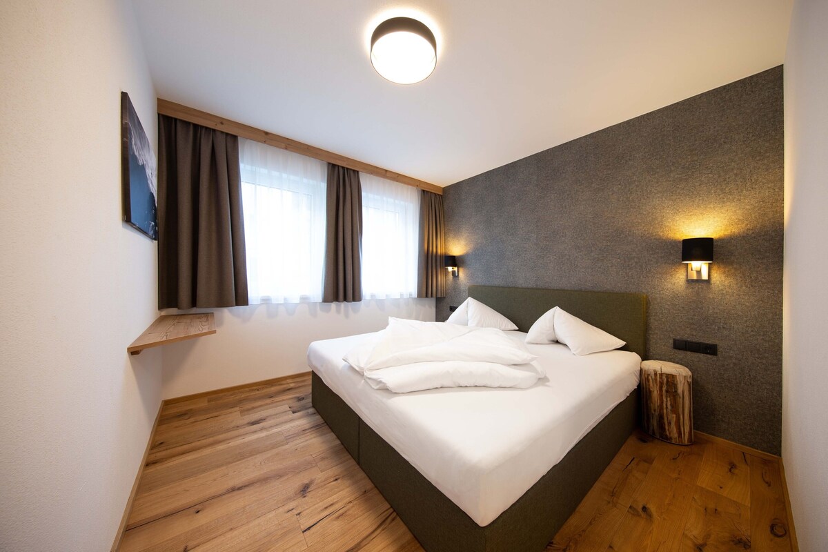 Una habitación de hotel moderna con una cama grande, suelo de madera, un banco empotrado y vistas de la ciudad a través de la ventana.