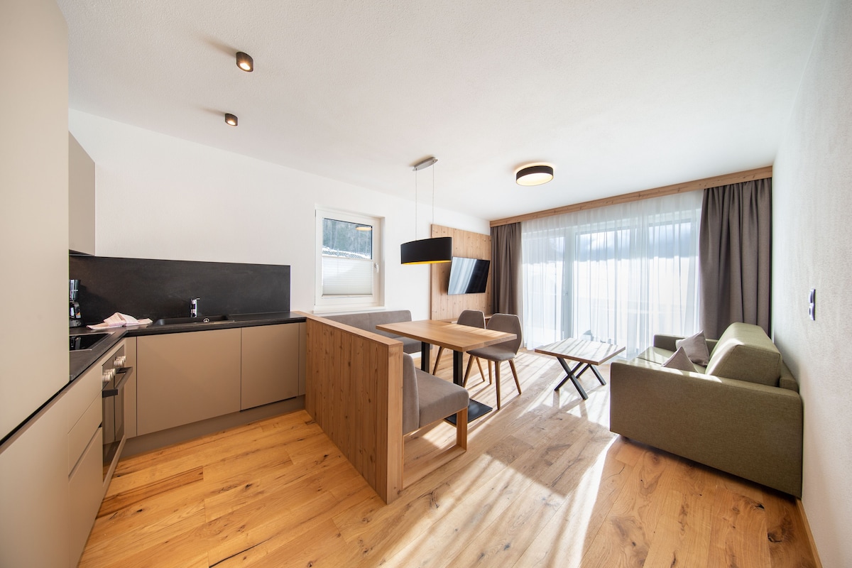 Una cocina moderna con armarios de madera, un comedor con mesa y sillas, y una sala de estar con sofá y televisor.