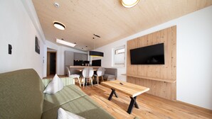 Un salon moderne avec une table à manger en bois, un canapé vert et un téléviseur à écran plat fixé à un mur en bois.