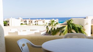 A balcony with a table and chairs, overlooking a beach and buildings. - CABO Stunner~Ocean View Beach Condo with Gorgeous Sunsets Sleep 6+ (Cabo San Lucas)