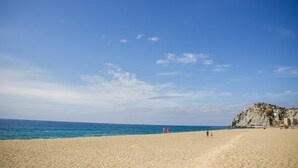 A wide sandy beach with a clear blue sky and a rocky cliff in the background. - CABO Stunner~Ocean View Beach Condo with Gorgeous Sunsets Sleep 6+ (Cabo San Lucas)