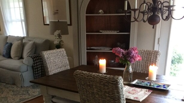 A dining area with a dark wooden table, wicker chairs, and a chandelier. - Charming Edgartown home with wrap around porch (Edgartown)