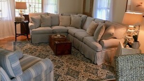 A living room with a sectional sofa, a patterned rug, a side table with a lamp, and a chair. - Charming Edgartown home with wrap around porch (Edgartown)