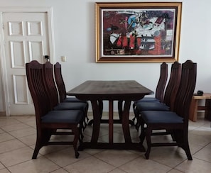 A dining area with a rectangular table and six chairs, a framed abstract painting on the wall, and a white door in the background.