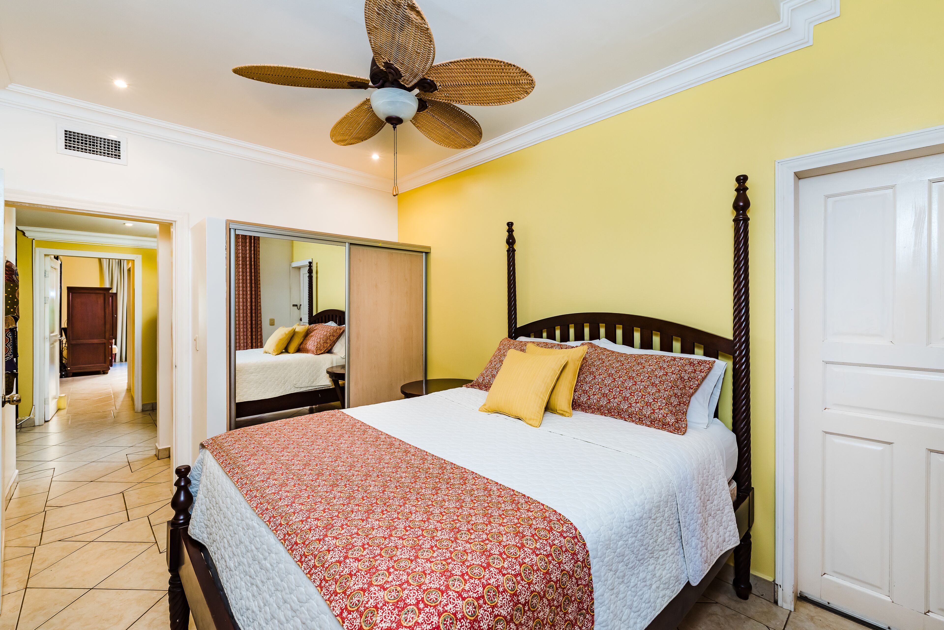 A bedroom with a bed, a ceiling fan, a mirror, and a door.