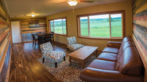 A cozy room with a wooden floor, a brown leather couch, a patterned rug, a wooden coffee table, and a dining table with chairs. - Secluded 6 acre home near the Henry's Fork River. (Ashton)