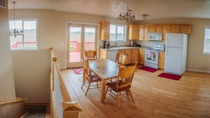 A kitchen with wooden cabinets, a dining table, chairs, a microwave, a refrigerator, and a view of a red deck through a glass door. - Secluded 6 acre home near the Henry's Fork River. (Ashton)