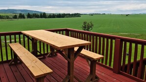 A wooden deck with a picnic table and benches overlooking a green field. - Secluded 6 acre home near the Henry's Fork River. (Ashton)