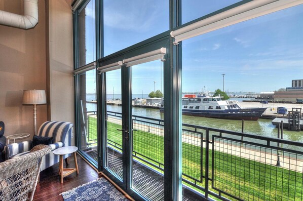 Enjoy a waterfront view from this spacious balcony with comfortable seating and large windows.