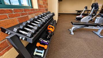Une salle de sport équipée d’un banc de développé couché, d’haltères et d’appareils de cardio.