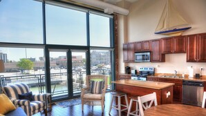 A spacious living area with a large window, a kitchen with wooden cabinets, and a dining area with a round table. - Upgrade Your Stay...On Sandusky Bay! (Sandusky)