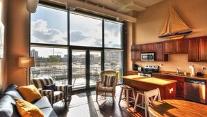 A spacious living area with a large window, a cozy seating area, and a kitchen with wooden cabinets and modern appliances. - Upgrade Your Stay...On Sandusky Bay! (Sandusky)