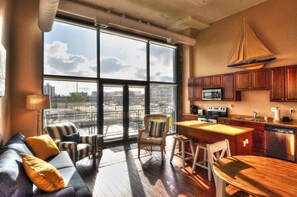 Relax in a spacious living area with a city view, featuring a sofa, armchairs, dining table, and kitchen.