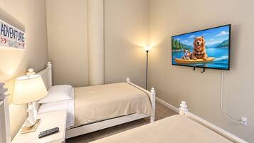 Un dormitorio con dos camas, una mesita de noche con lámpara, un televisor en la pared y una señalización sobre la cama.
