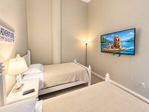 A bedroom with two beds, a nightstand with a lamp, a TV on the wall, and a sign above the bed.