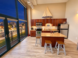 A modern kitchen with a large island, stainless steel appliances, and a view of a cityscape at dusk.