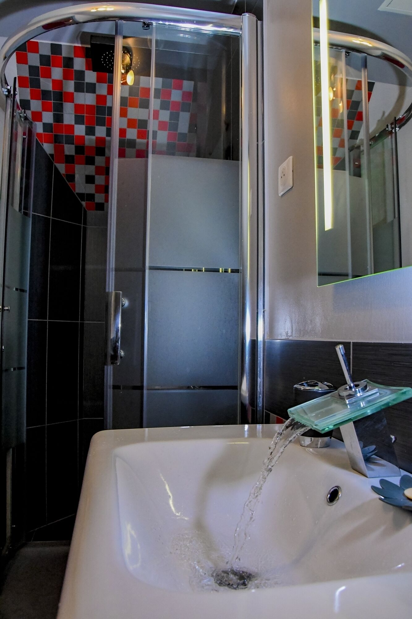 A bathroom with a glass shower enclosure, a white sink with a green soap dish, and a checkered tile wall.