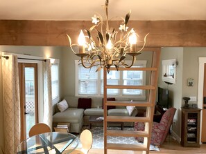 A living room with a chandelier, a glass table, a sofa, and a wooden bookshelf. - Cottage in Historic Irvington neighborhood near Convention Center and shops! (Portland)