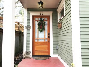 A house with a green siding exterior, a wooden front door with a wreath, a porch with a bench, and a sign that reads "Aug. Oregon Rogue Pacific Wonderland." - Cottage in Historic Irvington neighborhood near Convention Center and shops! (Portland)