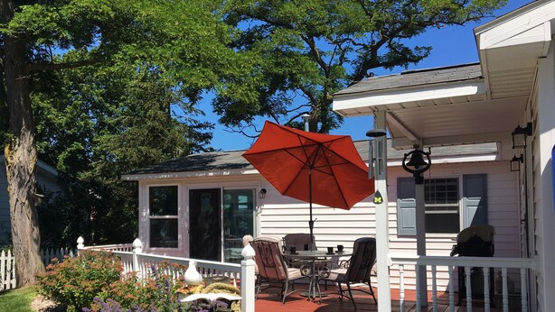 A house with a covered porch, a dining table, chairs, and a red umbrella. - BeachFrontRental-Tennis court&playground directly across the street!DogsWelcome (Elk Rapids)